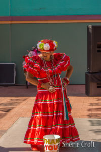 A senior woman in a festive, red Mexican dress and flowered hat dances in Market Square, San Antonio, Texas.